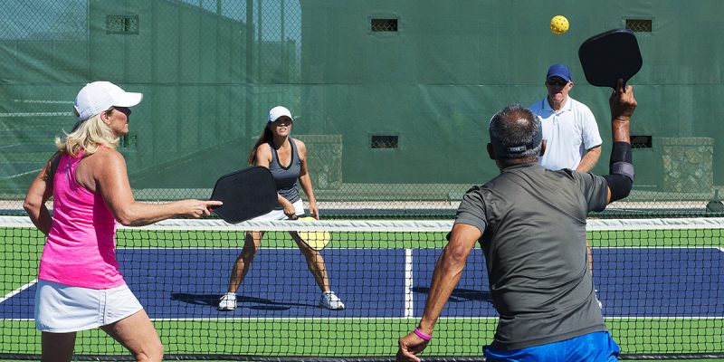 colorful action image of two couples playing a game of pickleball