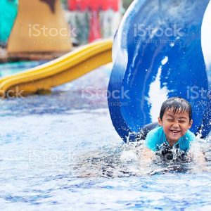 Cute asian boy having fun splashing into pool after going down water slide