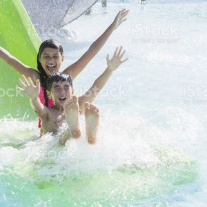 Children at water park, going down water slide.  9 and 12 years, mixed race Caucasian / Pacific Islander.